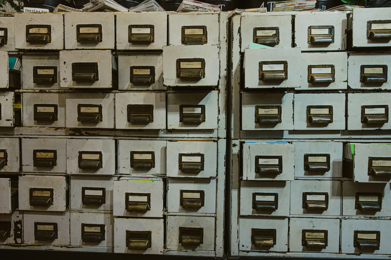 A wall of old painted card-catalogue drawers, each with a handwritten label in a brass holder.