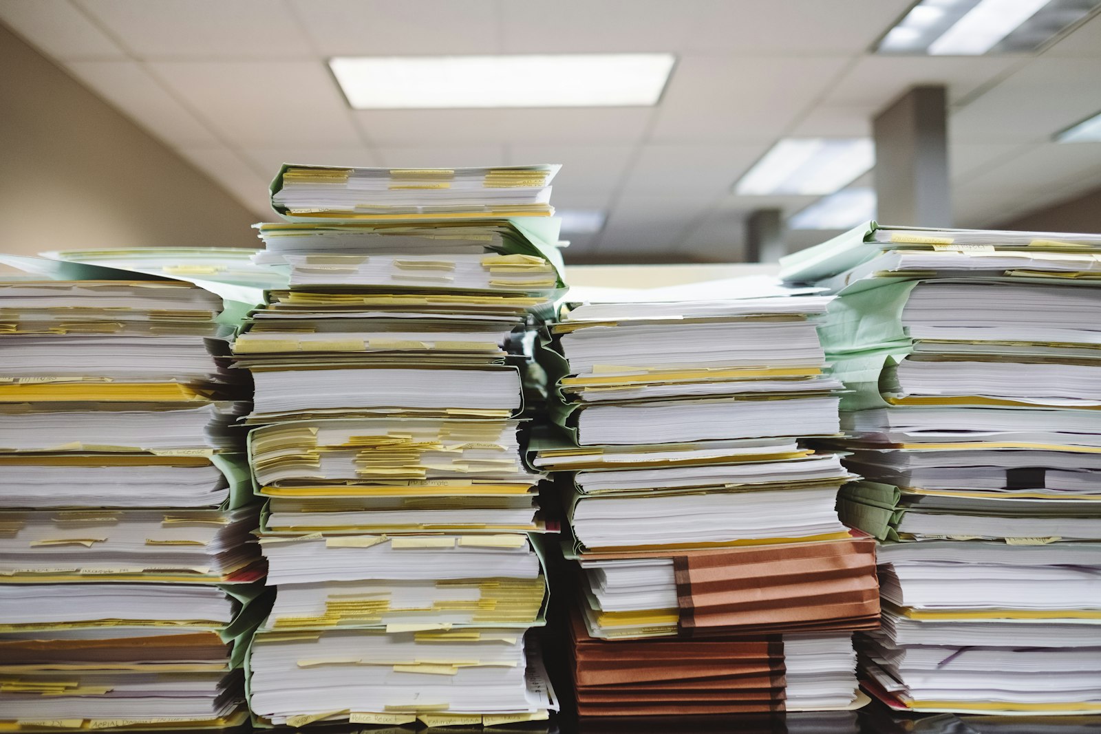 Four tall stacks of tabbed case files on a desk under office ceiling lights, one folder labelled Police Report.